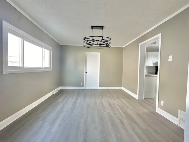 spare room featuring ornamental molding, an inviting chandelier, a textured ceiling, and light wood-type flooring