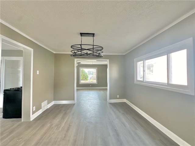 unfurnished dining area with wood-type flooring, a textured ceiling, crown molding, and an inviting chandelier