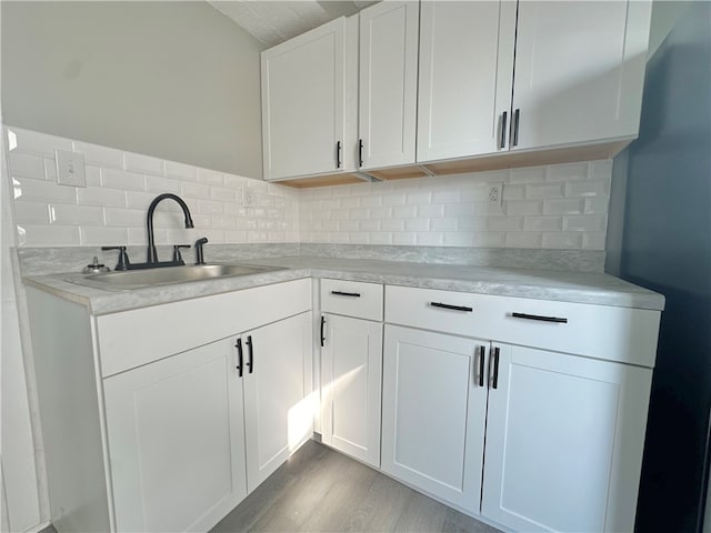 kitchen with sink, light wood-type flooring, white cabinets, and backsplash