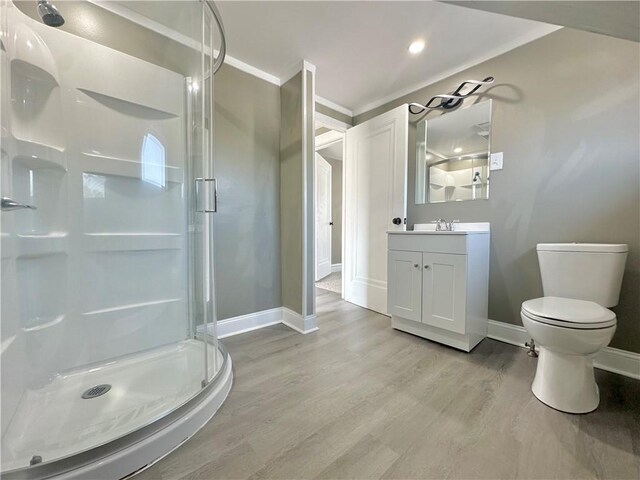 bathroom with hardwood / wood-style flooring, a shower with shower door, toilet, vanity, and crown molding