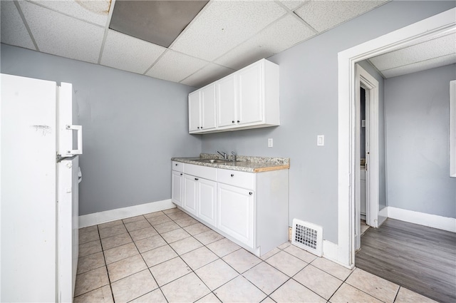 kitchen with white cabinetry, light hardwood / wood-style floors, a paneled ceiling, white refrigerator, and sink