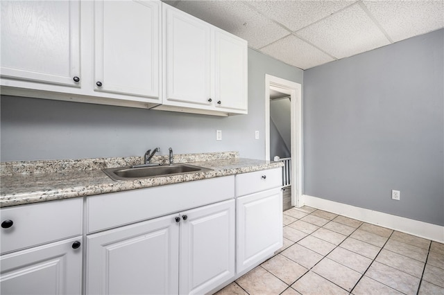 kitchen with sink, a drop ceiling, light tile patterned floors, and white cabinets