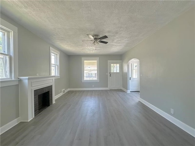 unfurnished living room with a fireplace, wood finished floors, arched walkways, and ceiling fan