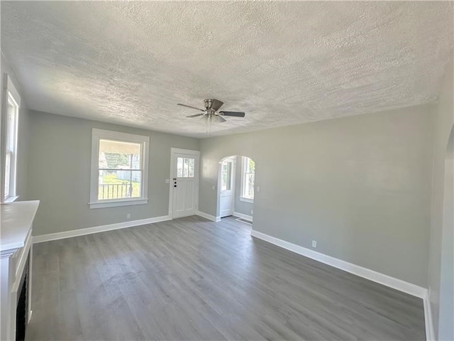 unfurnished living room featuring a textured ceiling, plenty of natural light, ceiling fan, and dark wood-type flooring