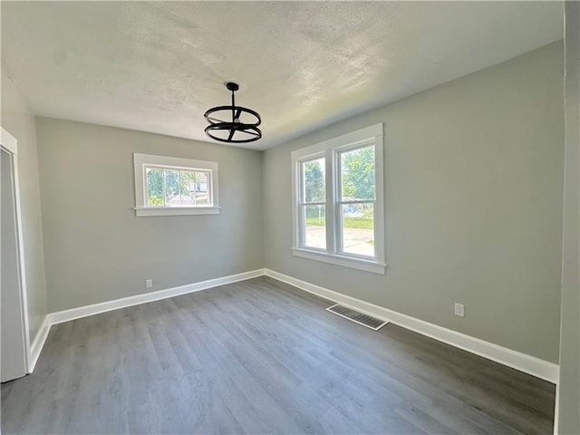 empty room with an inviting chandelier, a healthy amount of sunlight, a textured ceiling, and wood-type flooring