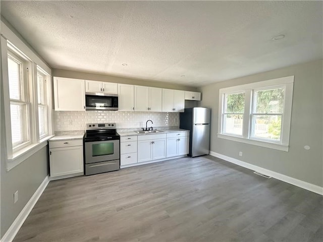 kitchen featuring white cabinetry, sink, backsplash, appliances with stainless steel finishes, and light wood-type flooring