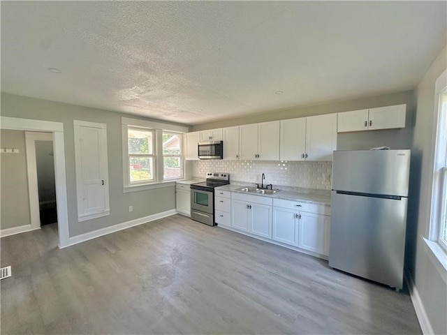 kitchen featuring sink, decorative backsplash, light wood-type flooring, white cabinetry, and stainless steel appliances