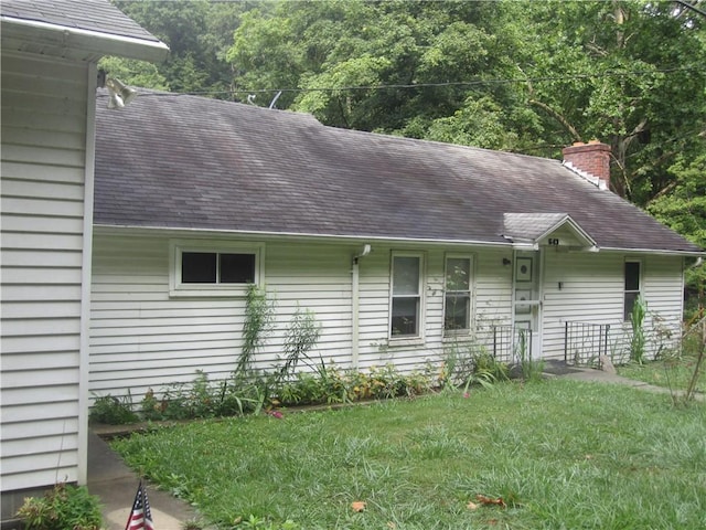 exterior space featuring a shingled roof, a chimney, and a front yard