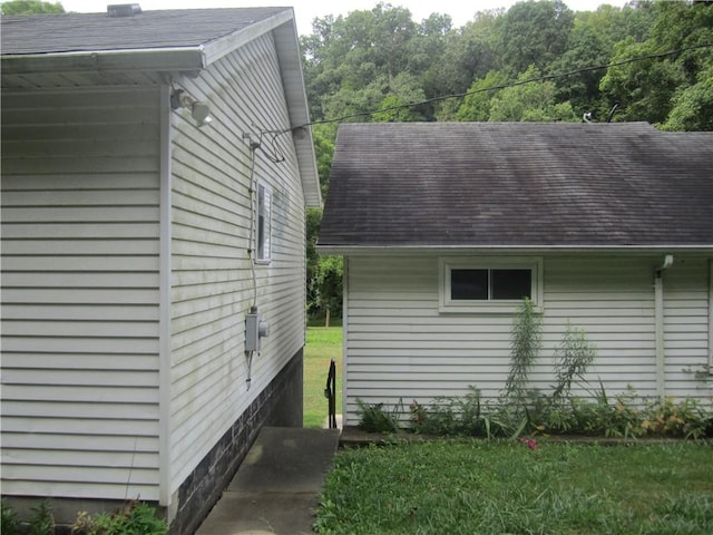 view of side of home with roof with shingles and a lawn