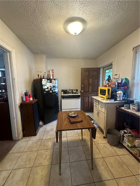 kitchen with light brown cabinetry, black fridge, white gas range oven, a textured ceiling, and light tile patterned floors