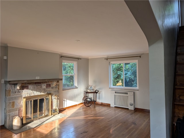 unfurnished living room with a stone fireplace, radiator heating unit, wood-type flooring, and ornamental molding