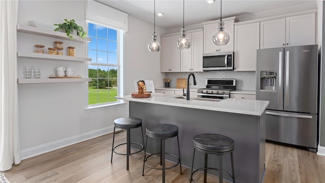 kitchen featuring appliances with stainless steel finishes, a breakfast bar area, a center island with sink, white cabinets, and light hardwood / wood-style floors