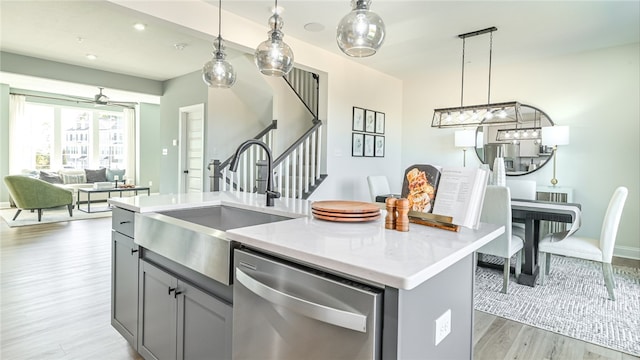 kitchen featuring light wood-type flooring, pendant lighting, dishwasher, sink, and a center island with sink