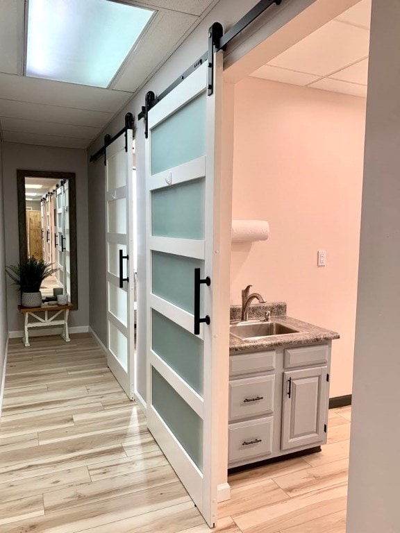 hallway featuring a drop ceiling, light hardwood / wood-style flooring, a barn door, and sink