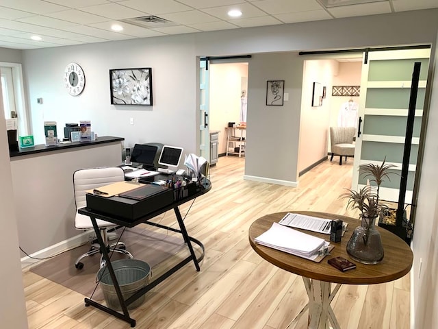 home office featuring light wood-type flooring, a drop ceiling, and a barn door