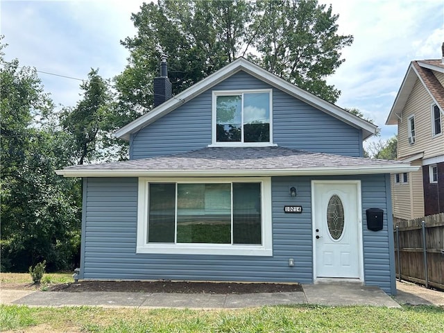 bungalow-style home with roof with shingles, a chimney, and fence