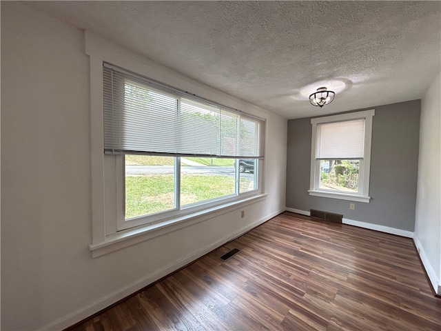 empty room with baseboards, wood finished floors, visible vents, and a textured ceiling