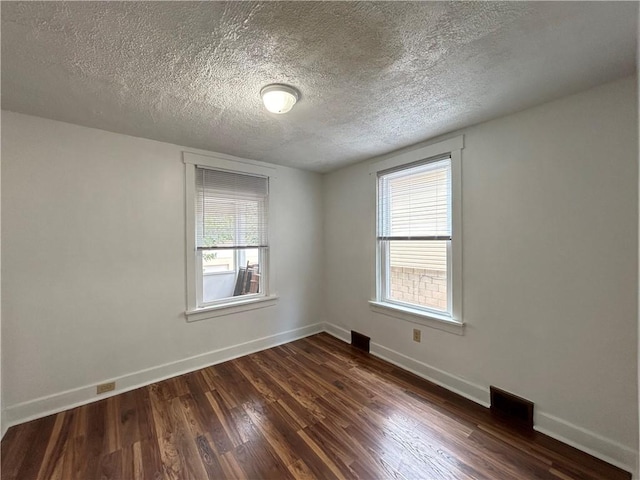 spare room with visible vents, baseboards, a textured ceiling, and dark wood-style floors