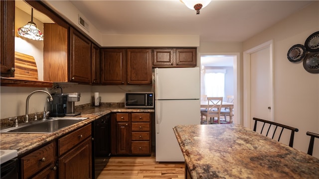 kitchen featuring white fridge, light hardwood / wood-style floors, black dishwasher, a kitchen breakfast bar, and sink