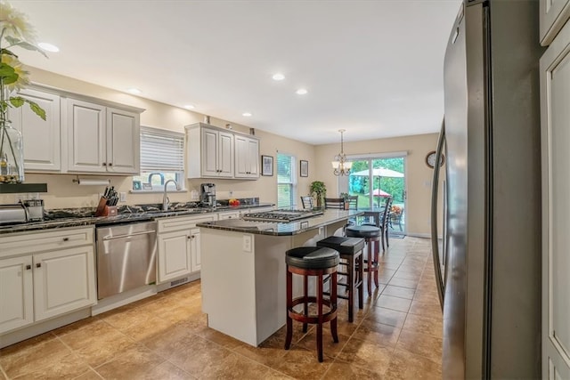 kitchen featuring a kitchen bar, a center island, hanging light fixtures, white cabinetry, and stainless steel appliances