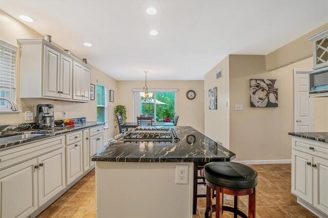 kitchen with a kitchen island, stainless steel gas stovetop, dark stone countertops, pendant lighting, and sink