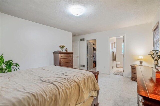 bedroom featuring ensuite bath, light carpet, a textured ceiling, and a walk in closet