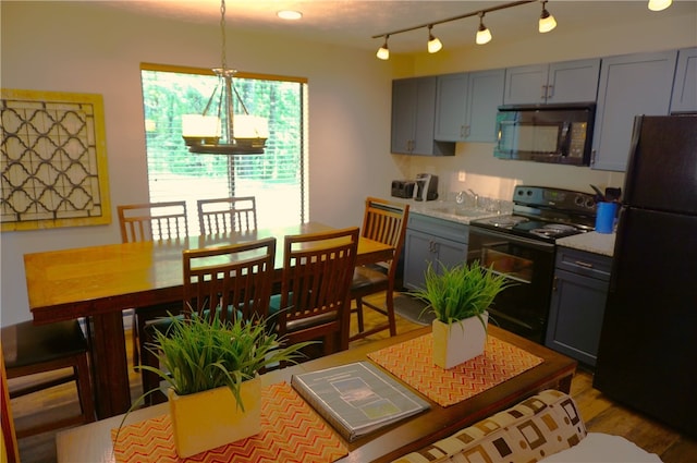 kitchen with light countertops, hanging light fixtures, gray cabinetry, light wood-style floors, and black appliances