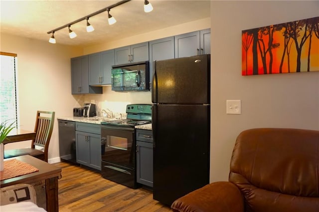 kitchen featuring a sink, black appliances, wood finished floors, and gray cabinetry