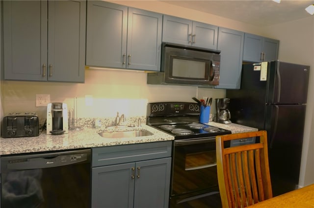 kitchen featuring black appliances, light stone counters, a sink, and gray cabinetry