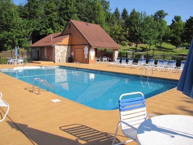 community pool with a patio area, fence, and an outbuilding