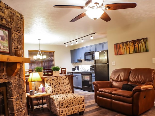 living area with dark wood-style flooring, a stone fireplace, a textured ceiling, and ceiling fan with notable chandelier