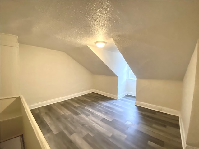 additional living space featuring dark wood-type flooring, vaulted ceiling, and a textured ceiling