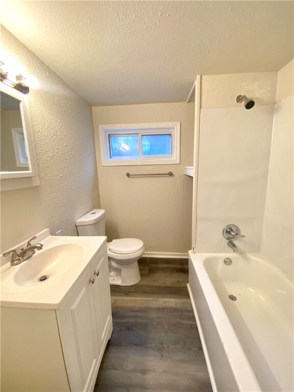 full bathroom with shower / bathing tub combination, a textured ceiling, toilet, vanity, and wood-type flooring