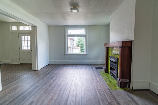 unfurnished living room with hardwood / wood-style flooring, a baseboard heating unit, and a tiled fireplace