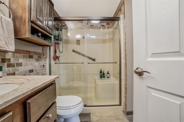 bathroom featuring vanity, a shower with door, tasteful backsplash, and toilet