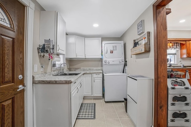 kitchen featuring stacked washer / dryer, sink, light tile patterned floors, and white cabinetry