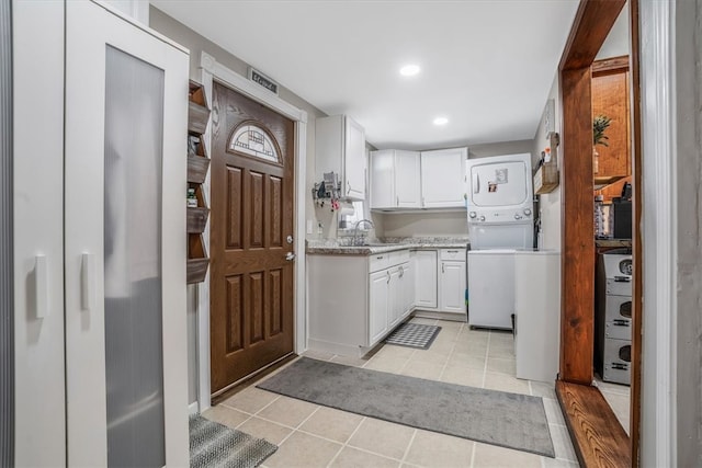 kitchen featuring light tile patterned flooring, white cabinetry, stacked washer and clothes dryer, and light stone countertops