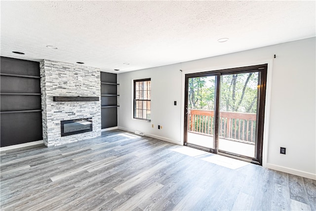 unfurnished living room with built in shelves, a textured ceiling, a stone fireplace, and hardwood / wood-style flooring