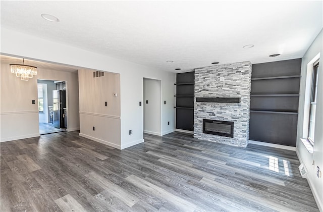 unfurnished living room with dark wood-type flooring, built in shelves, a fireplace, and a textured ceiling