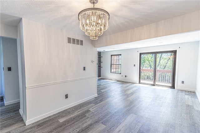 empty room featuring a notable chandelier, dark hardwood / wood-style flooring, and a textured ceiling