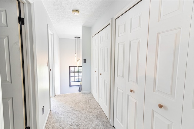 corridor featuring a textured ceiling and light colored carpet