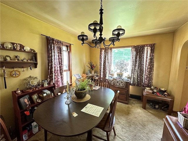 dining area with a chandelier, arched walkways, and light carpet