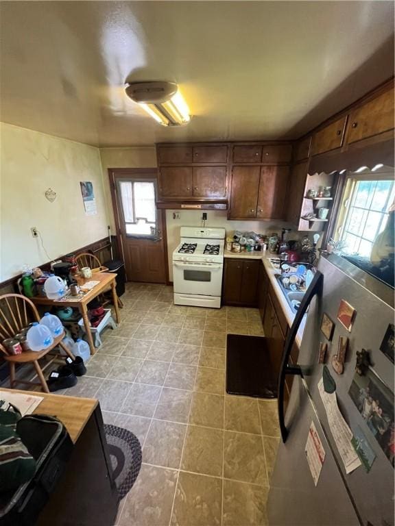 kitchen with light tile patterned floors, under cabinet range hood, light countertops, freestanding refrigerator, and white gas range