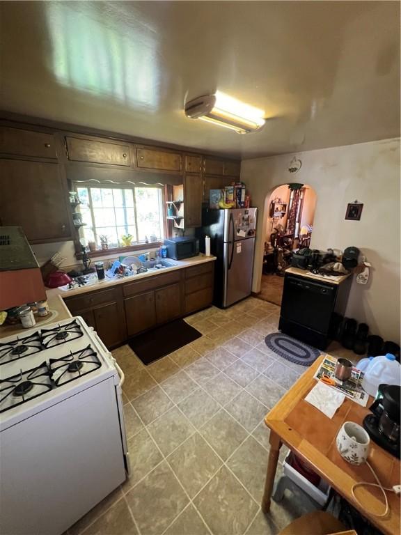 kitchen with arched walkways, gas range gas stove, light tile patterned floors, freestanding refrigerator, and black microwave