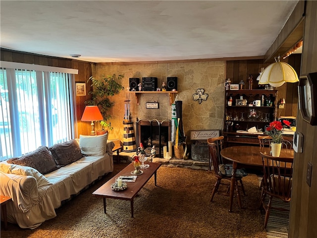 carpeted living room with a fireplace and wooden walls