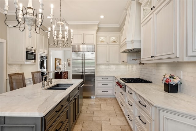 kitchen with hanging light fixtures, white cabinetry, stainless steel appliances, custom range hood, and a kitchen island with sink