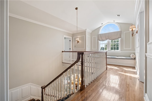 hall with light hardwood / wood-style floors, ornamental molding, and lofted ceiling