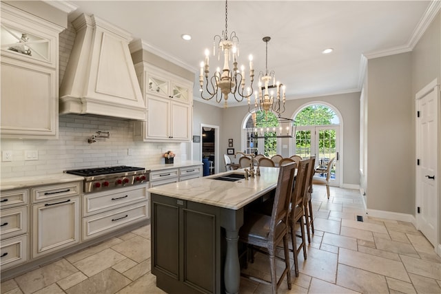 kitchen with a center island with sink, crown molding, stainless steel gas stovetop, premium range hood, and light stone counters