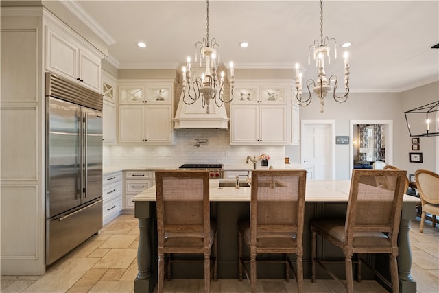 kitchen with a kitchen breakfast bar, ornamental molding, stainless steel built in refrigerator, and a center island with sink