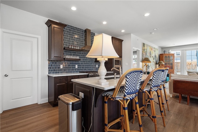 kitchen with a breakfast bar, dark brown cabinets, decorative backsplash, hardwood / wood-style flooring, and sink